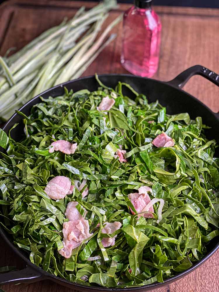thinly sliced collard greens mixed with bacon in a cast iron skillet