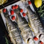fire roasted whole branzino on a pan with roasted cherry tomatoes