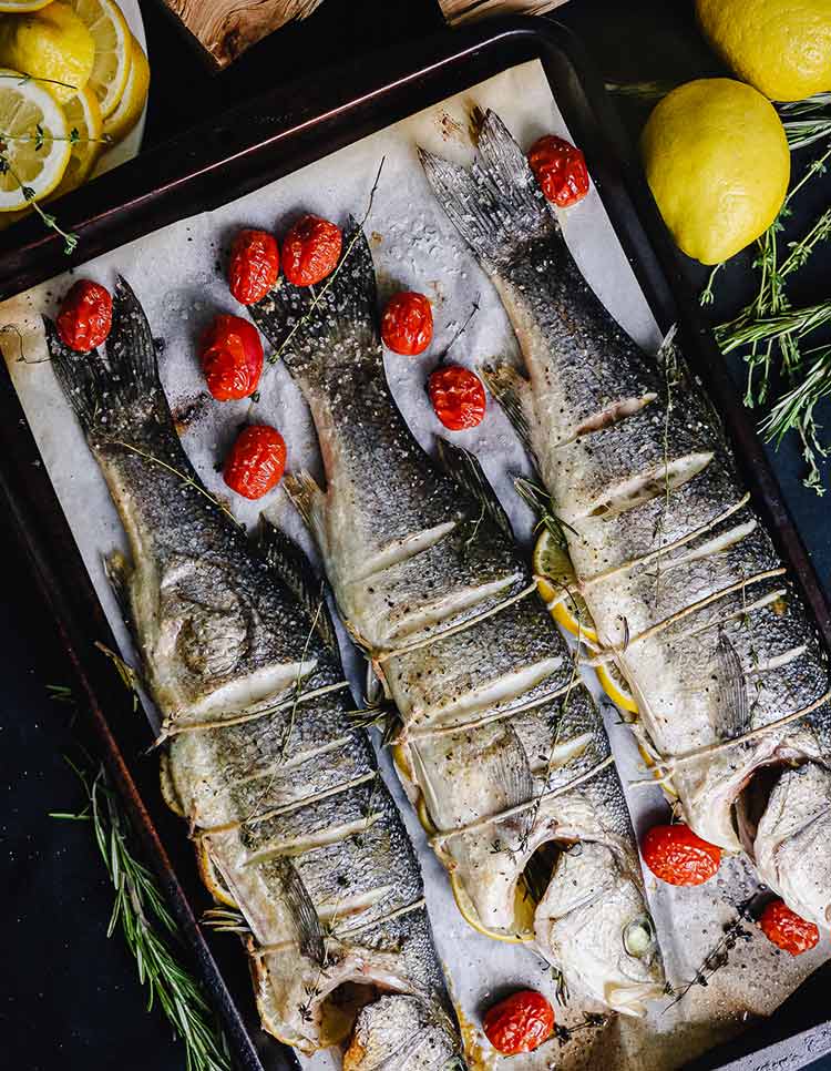 fire roasted whole branzino on a pan with roasted cherry tomatoes