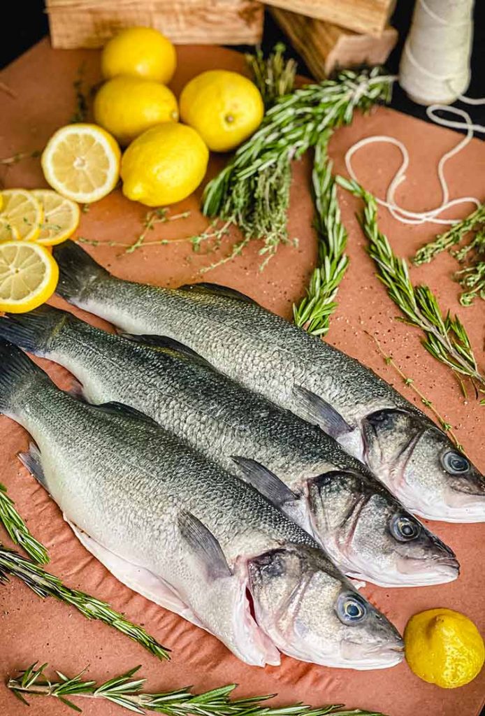 three silver fish on butcher paper, surrounded with lemon slices and rosemary