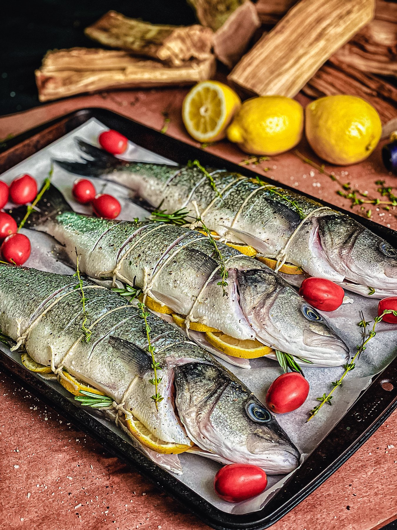 three fish and cherry tomatoes on sheet pan lined with parchment paper, ready to grill