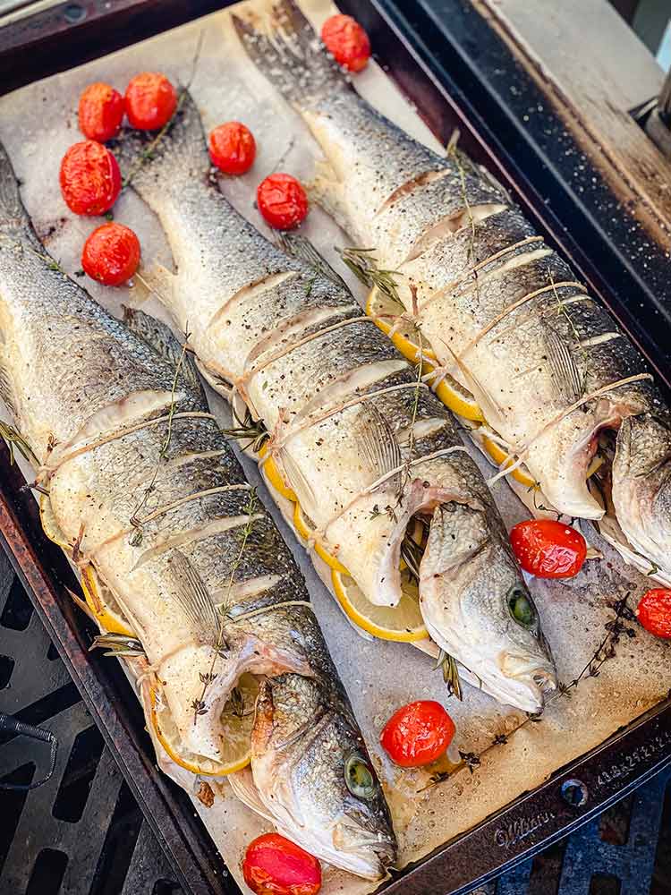 partially cooked fish and tomatoes rest in a sheet pan while grill is stoked to higher temperature