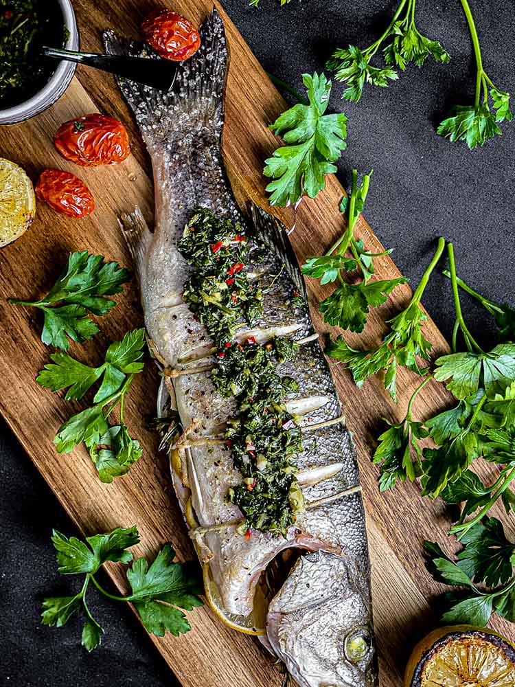 fire roasted whole branzino on a wood plank with roasted tomatoes, lemons and chimichurri