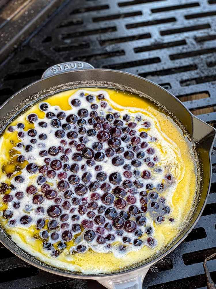 cast iron pan of blueberry cobbler on a grill