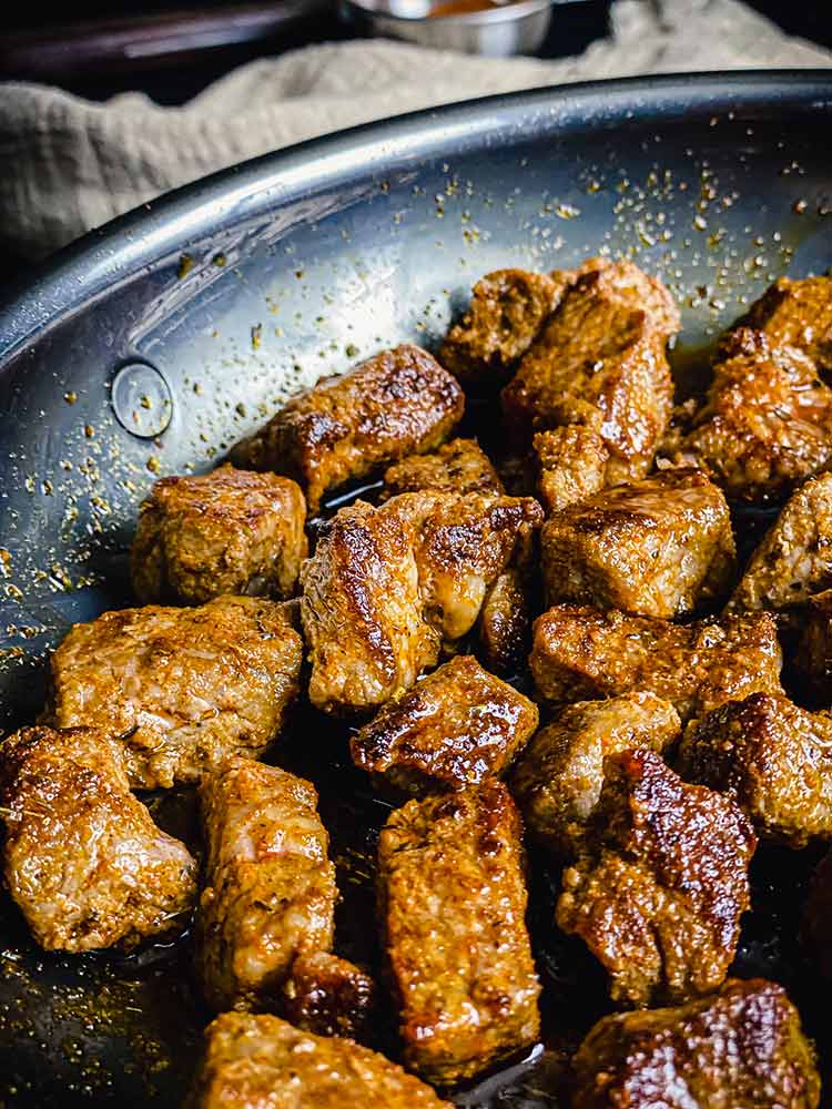 close up of bite-sized steak coated in butter and Cajun seasoning in frying pan