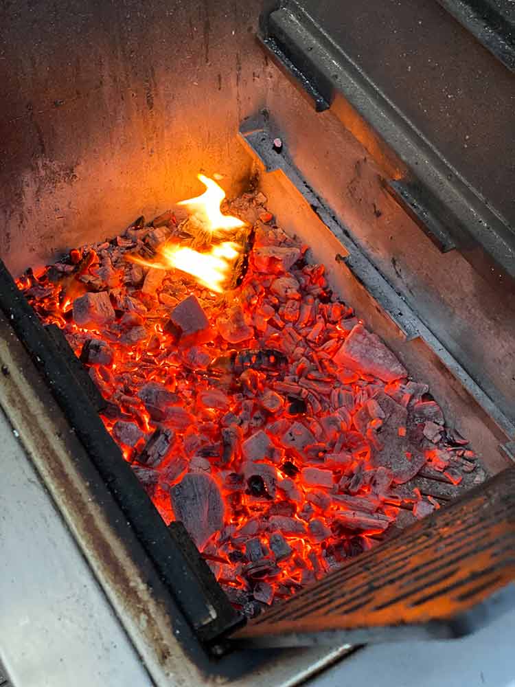 red hot coals with a flame in a stainless steel Kamado-style cooker