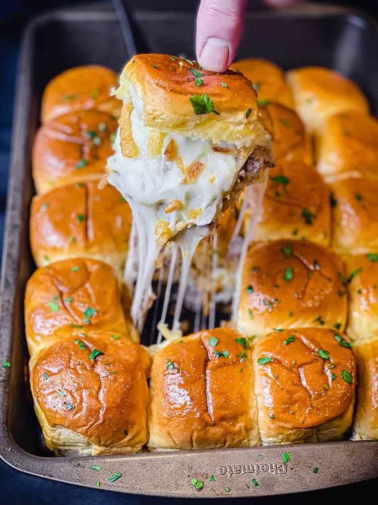 Removing a slider from the pan, with melted cheese, crispy fried onions, and steak 