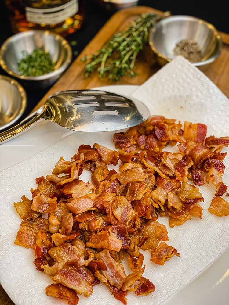 drained of fat with a slotted spoon, bacon rests on a paper towel
