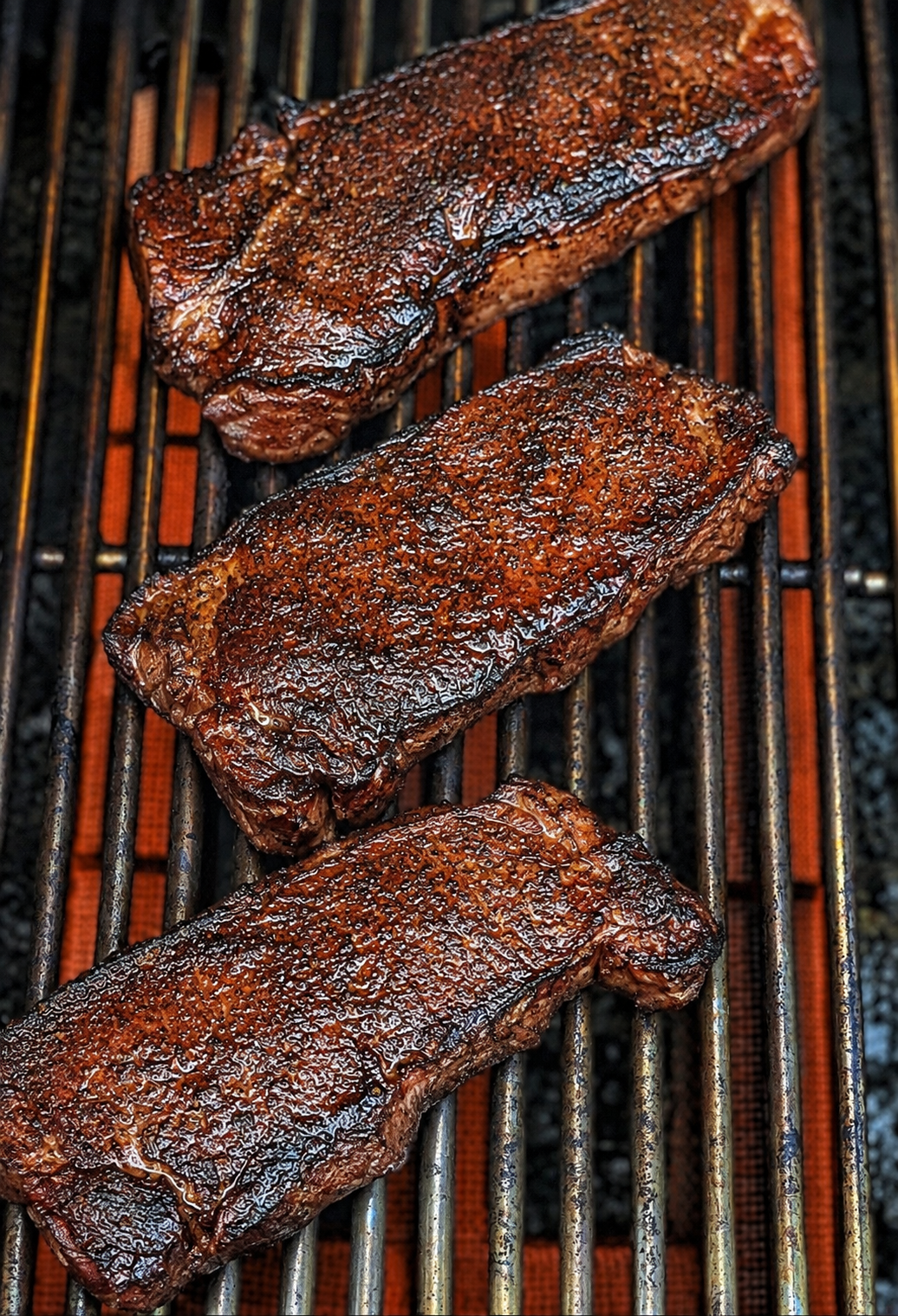 New York strip steaks grilling over high heat with a dark, caramelized crust