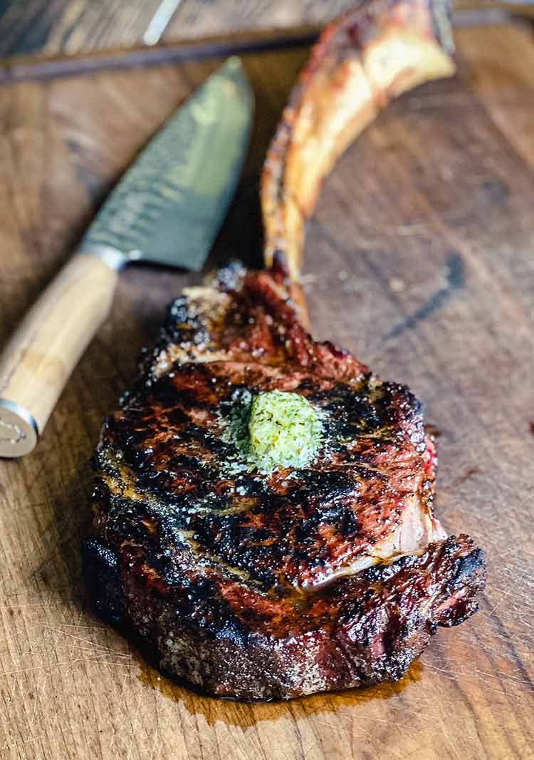 reverse seared steak with a pat of herb butter on a cutting board 
