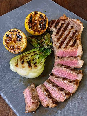 grill marks on steak sliced to show perfect rare doneness, on lemon halves and half of a bok choy  