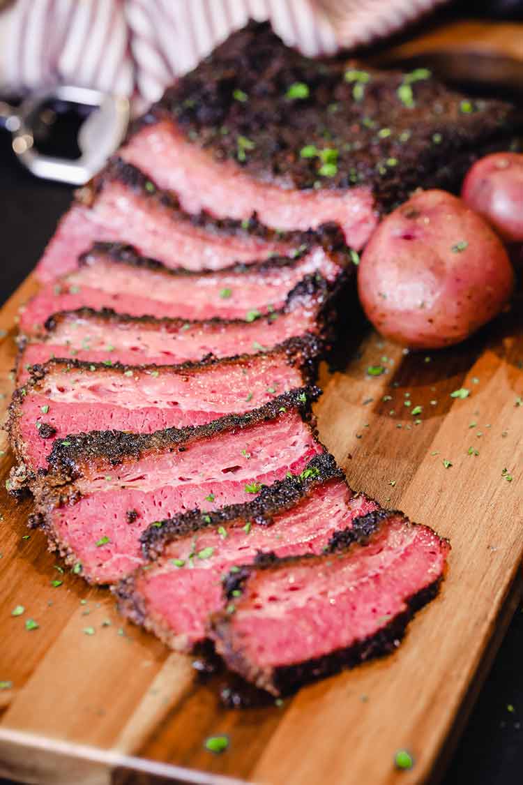 Smoked and beer braised corned beef on a cutting board with potatoes and a block of hickory 