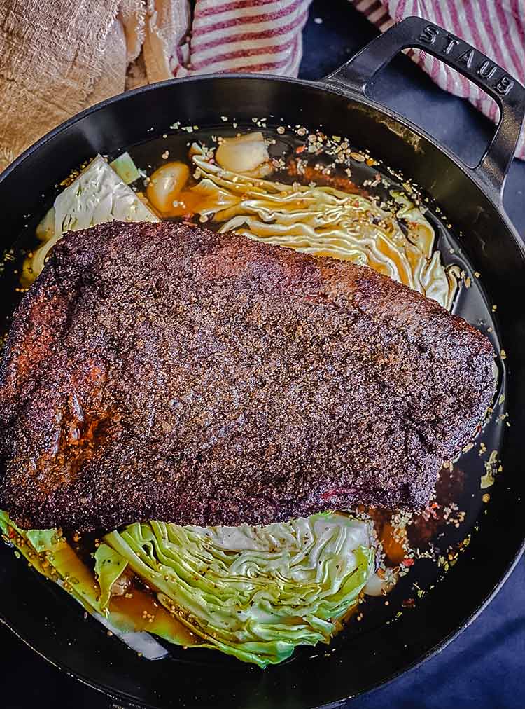 Smoked corned beef on a bed of cabbage semi-circles and potatoes with beer braise in an oven-safe pan
