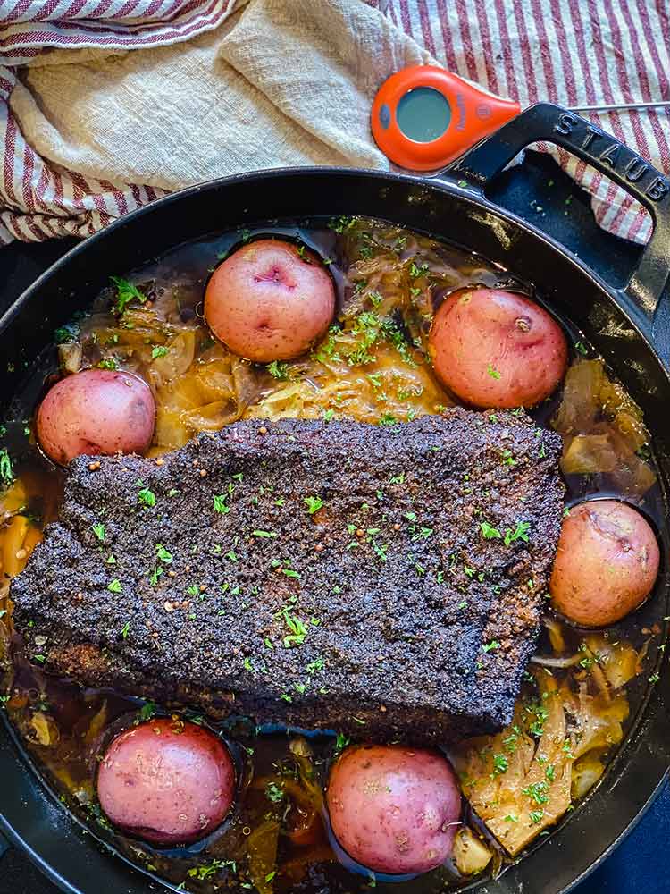 whole red potatoes added to cast iron pan containing beer-braised corned beef and cabbage
