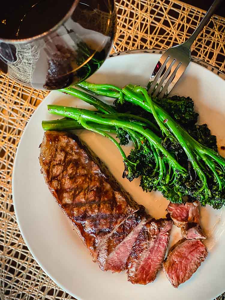 grilled broccolini on a plate next to a fork and wineglass