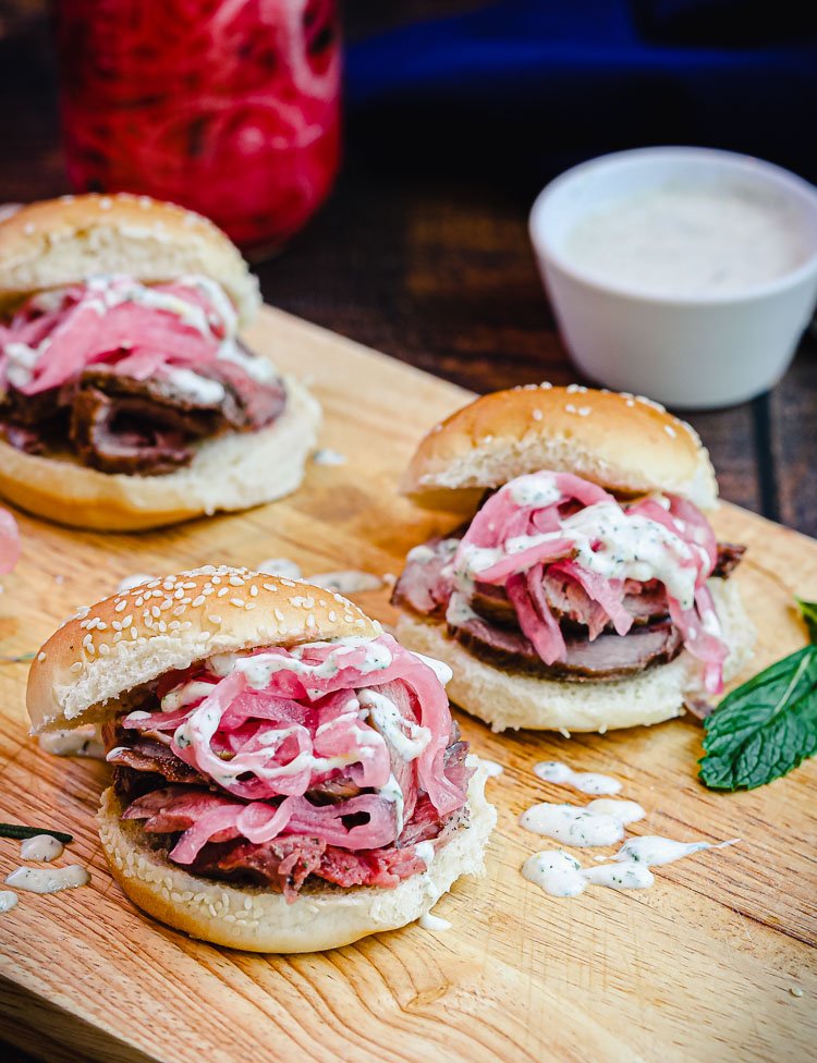 lamb sliders on cutting board with mint and greek sauce