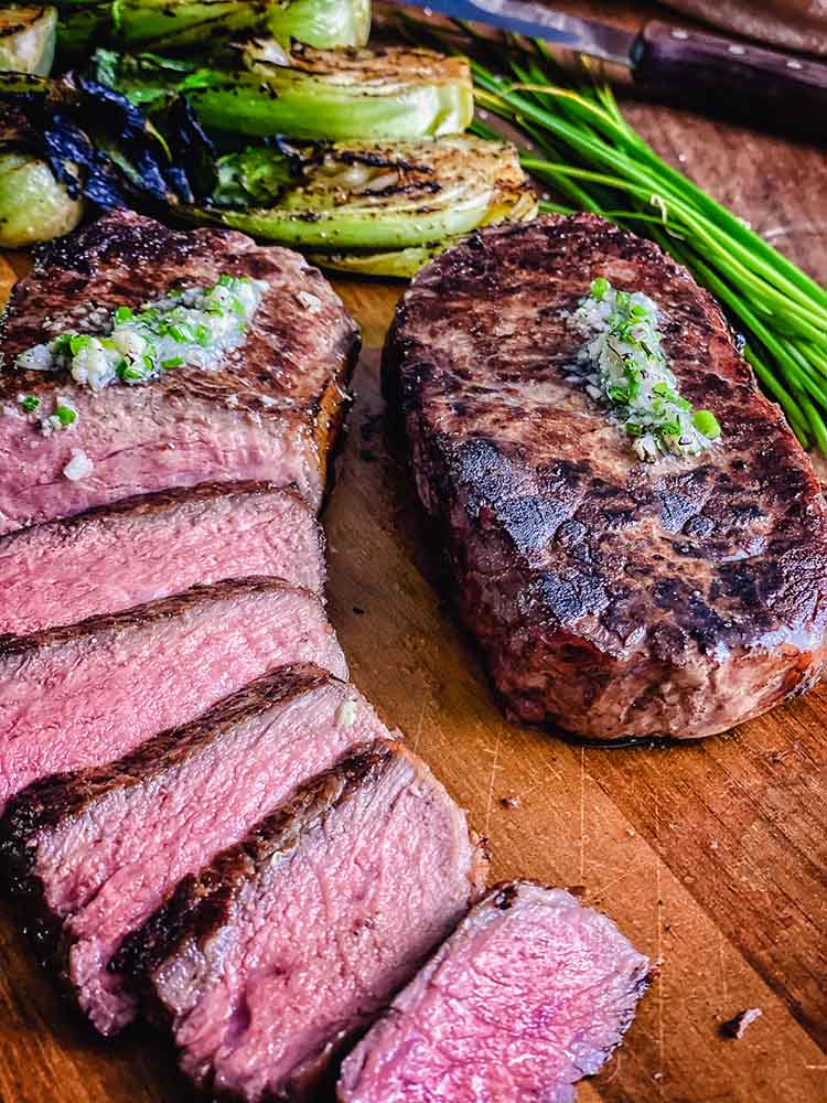 New York strip steak sliced and ready to serve, on a cutting board with bok choy