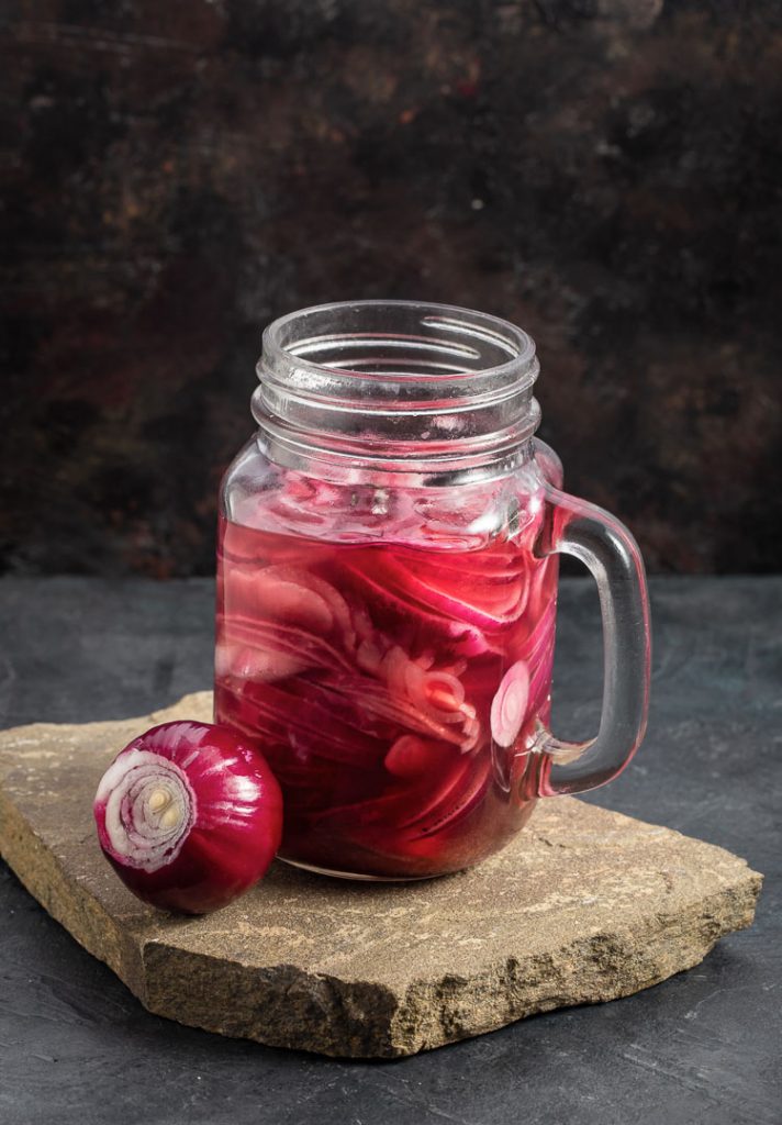 pickled red onions in a jar with a handle and whole red onion