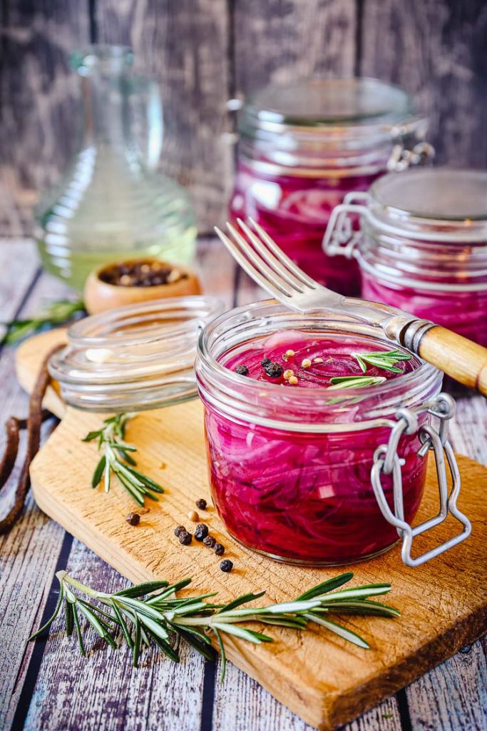 pickled red onions in a jar with rosemary on a cutting board
