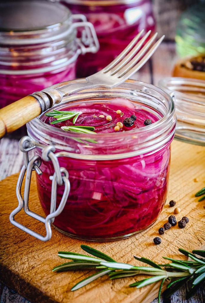 pickled red onions in a glass jar with peppercorns and fork