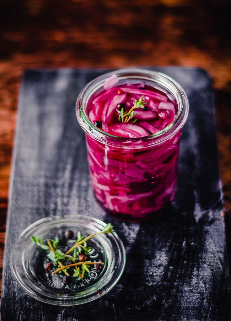 pickled red onions in a jar with some herbs next to them