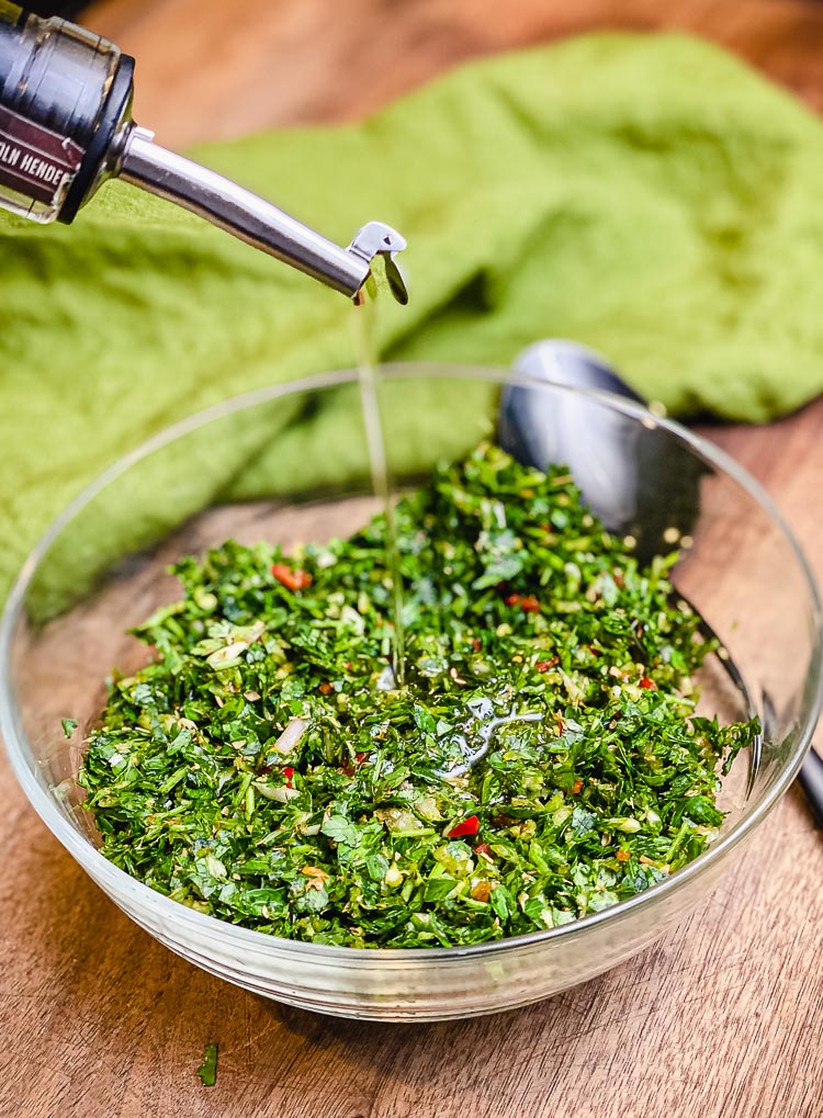 olive oil being poured into a bowl of chimichurri