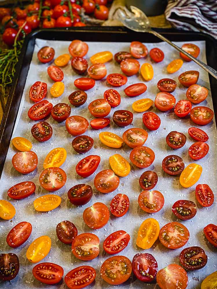 halved grape and cherry tomatoes in shades of red and yellow on a pan