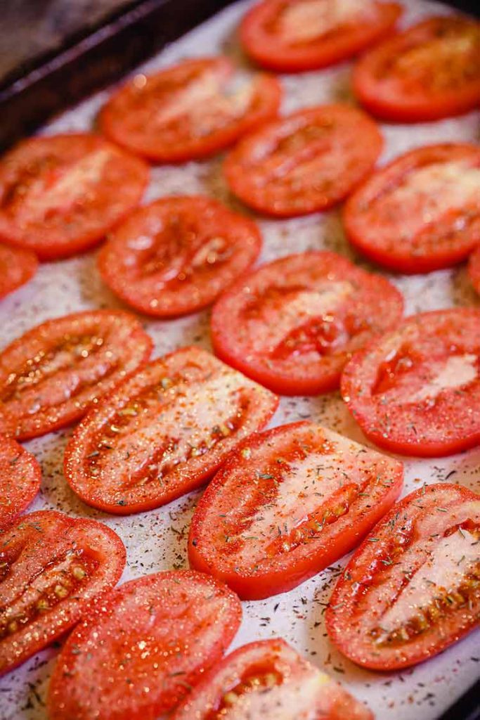 spices sprinkled on Roma tomatoes sliced and spread on pan