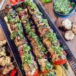 grilled chicken kabobs on a platter with chimichurri