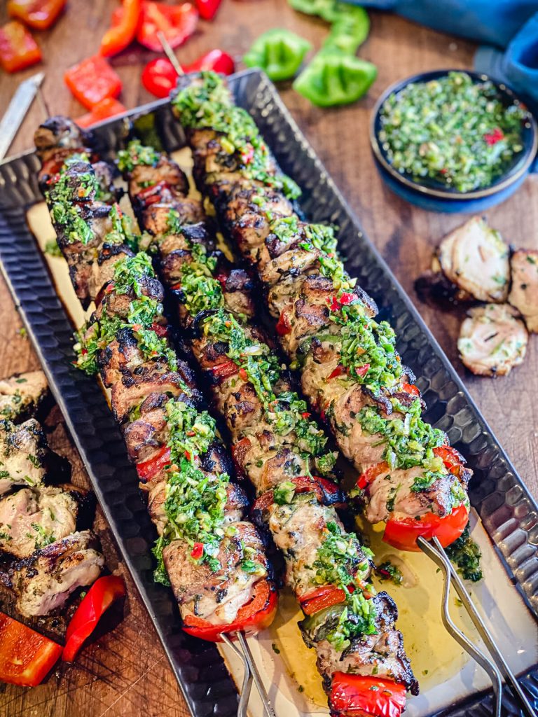 grilled chicken kabobs on a platter with chimichurri