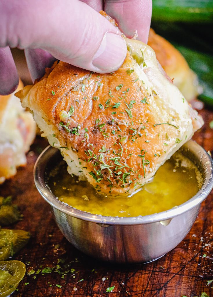 ham and cheese slider being dipped into a butter sauce