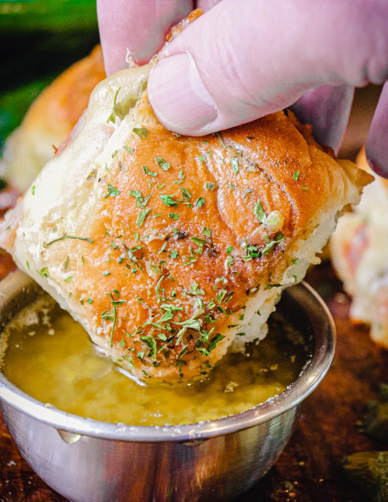 ham and cheese slider being dipped into a dijon butter sauce