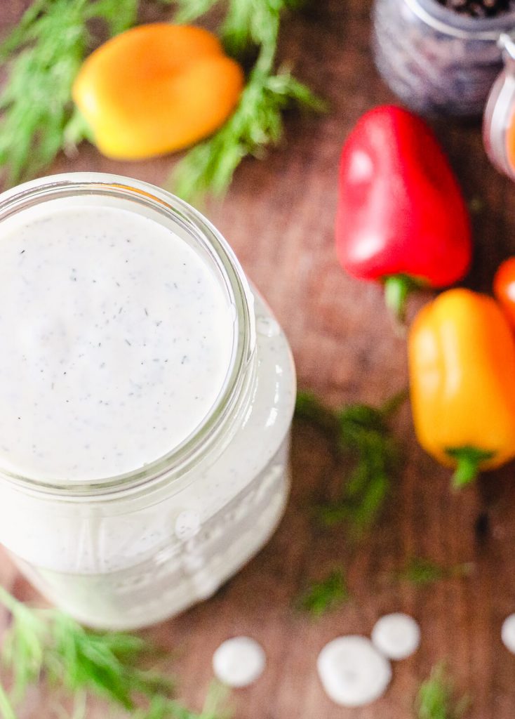 top view of a full jar of homemade ranch dressing with sweet peppers in the background