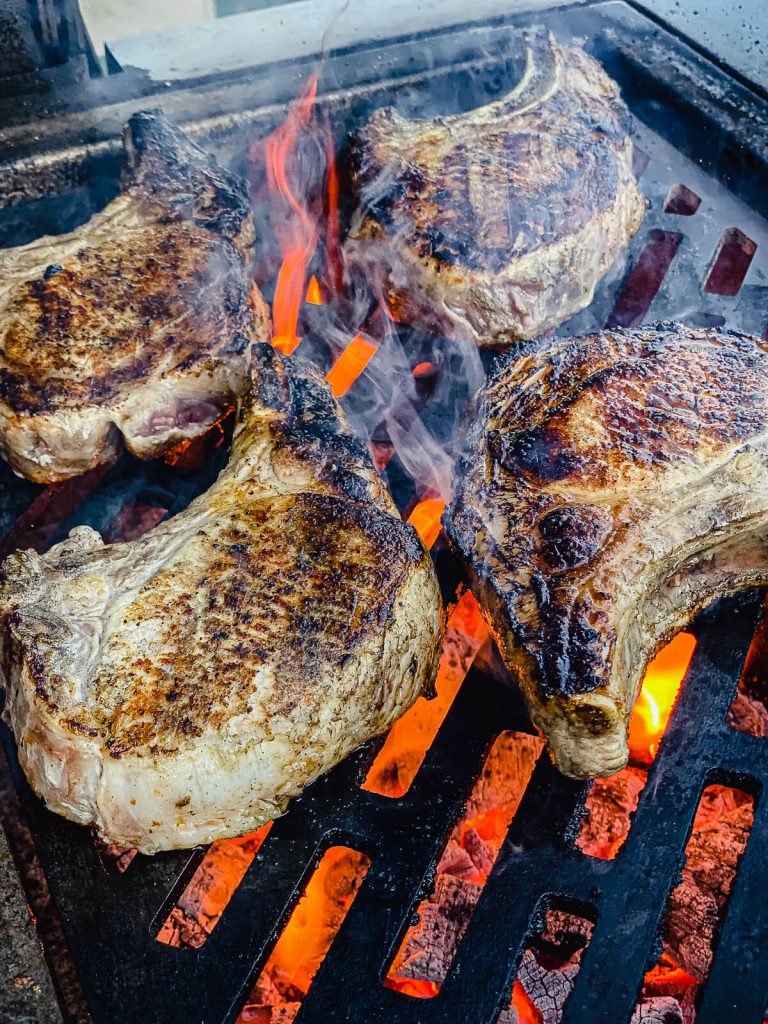 pork chops being grilled over charcoal