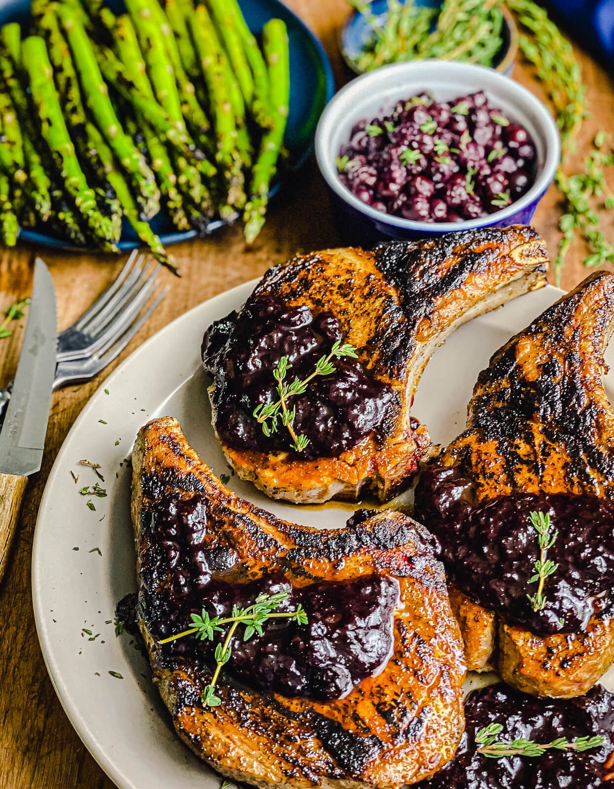 grilled pork chops with blueberry chipotle sauce on a plate with asparagus