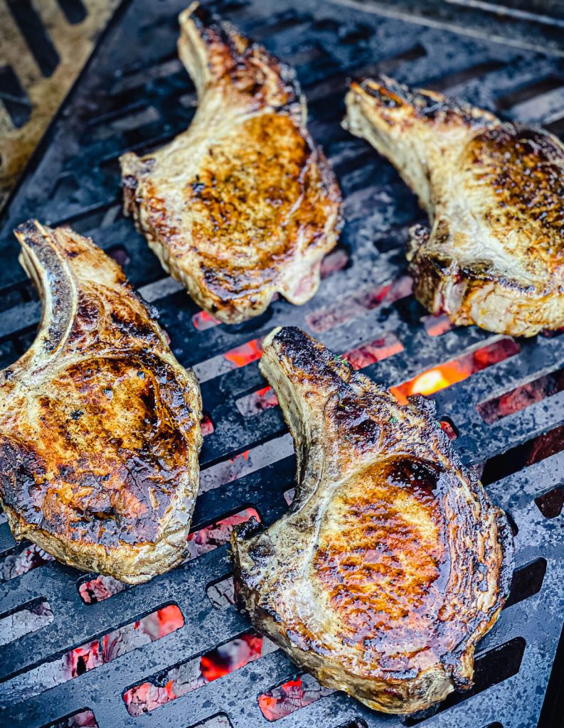 pork chops on a grill grate being cooked over charcoal