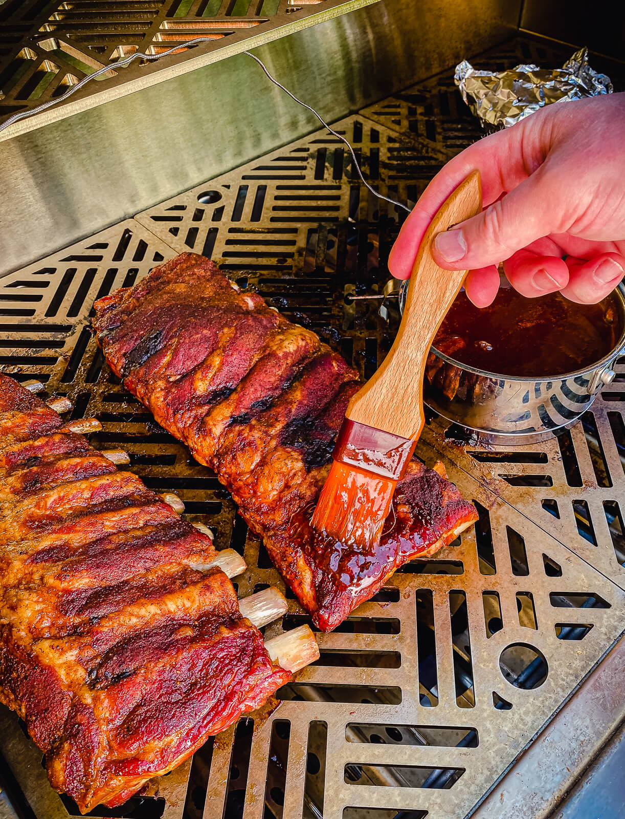 pork ribs on a gas grill having sauce applied to them