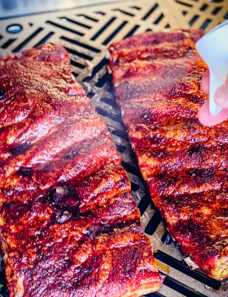 pork ribs on a gas grill being spritzed