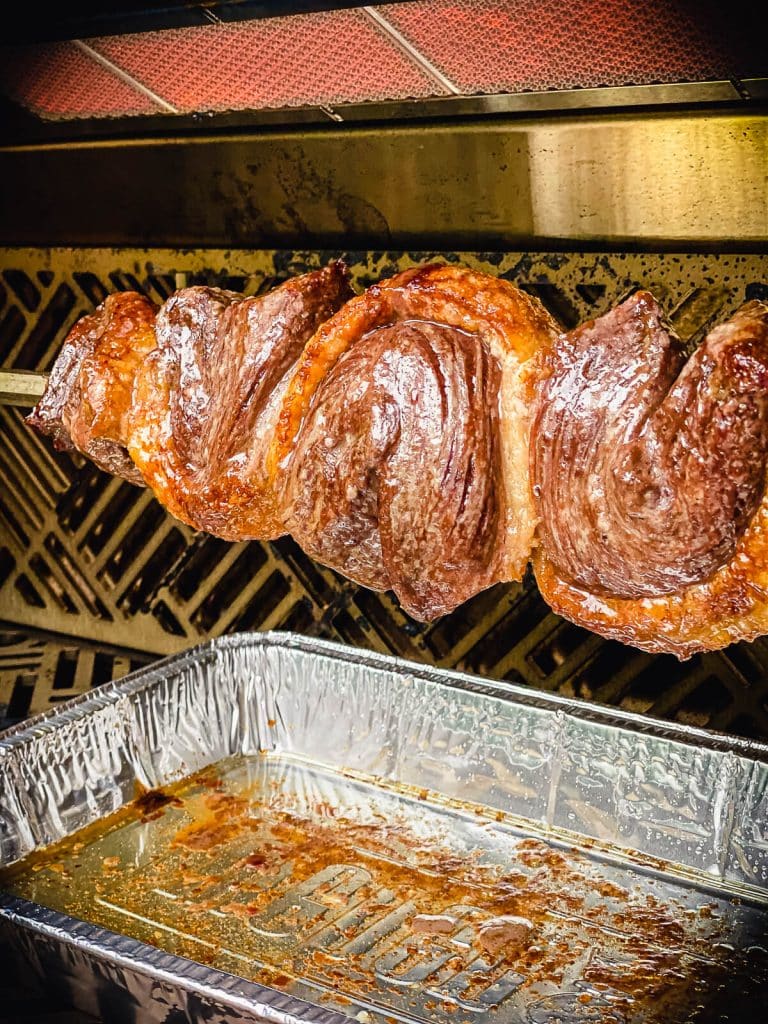picanha on a rotisserie being cooking on a grill