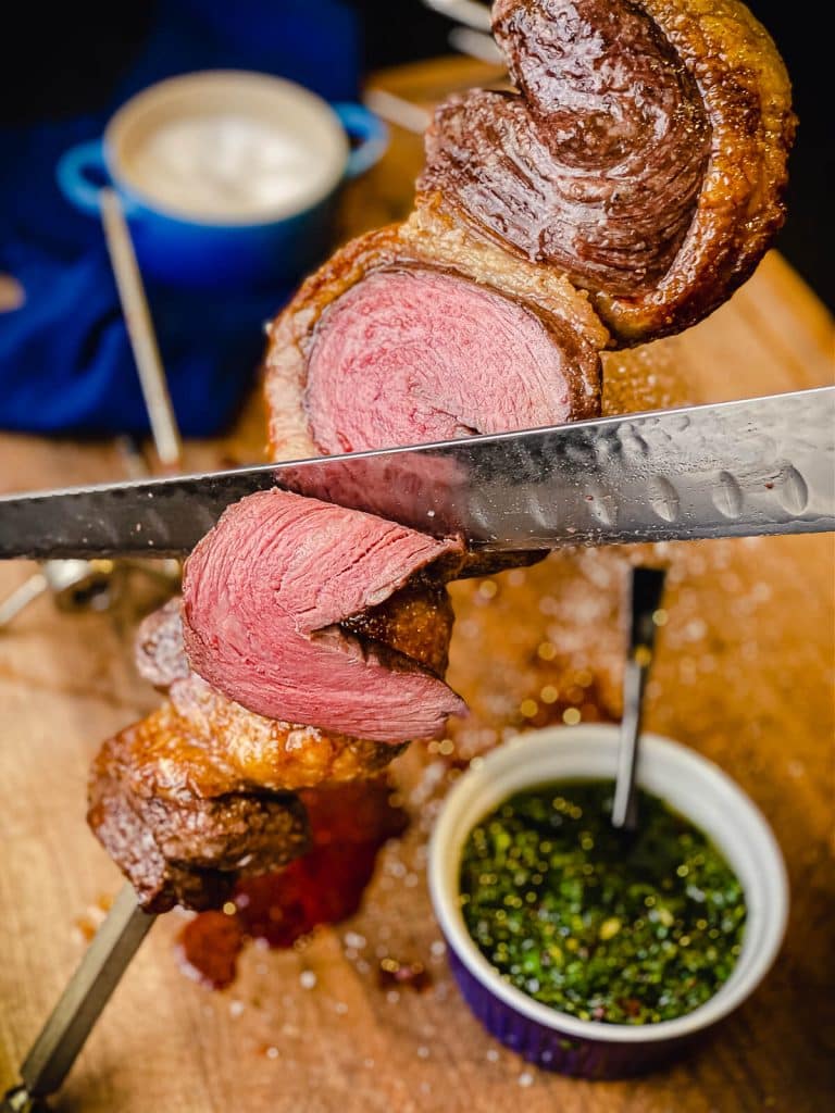 picanha being sliced off of a rotisserie spit