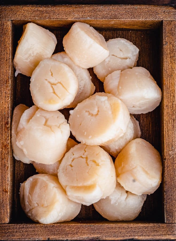 raw scallops piled in a wooden box