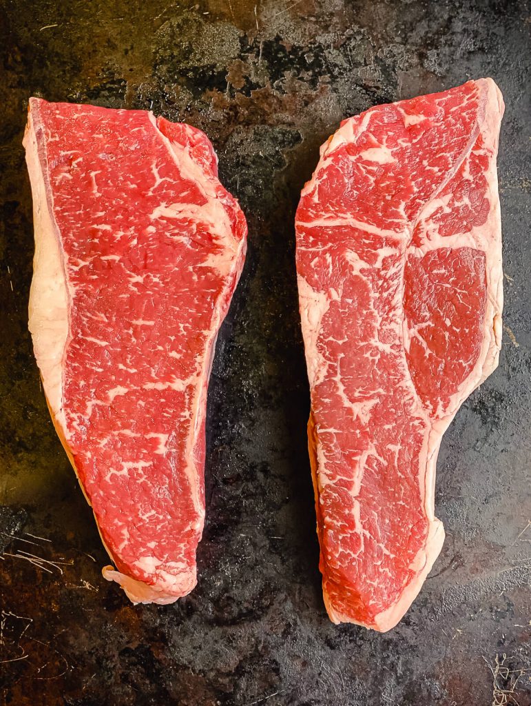 two strip steaks side by side on a black surface
