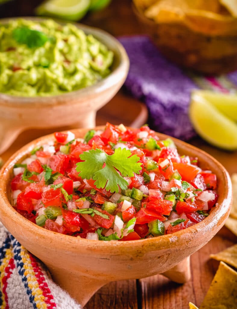 a wood bowl of pico de gallo and some limes on a table