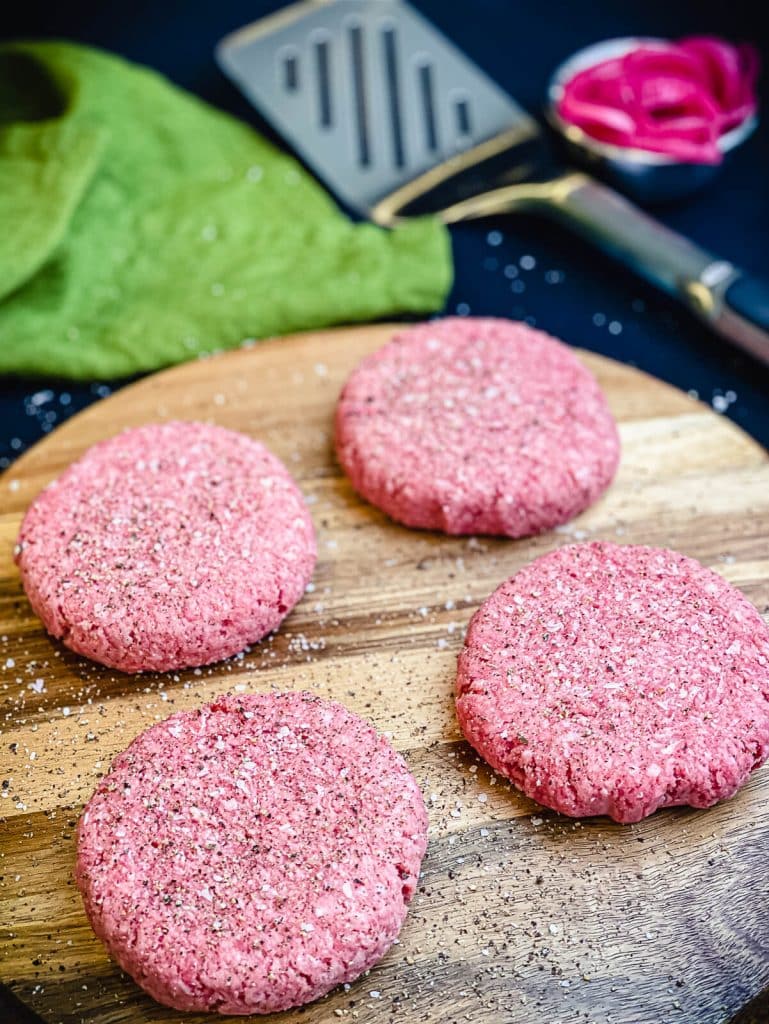 burger patties sitting on a cutting board with salt and pepper