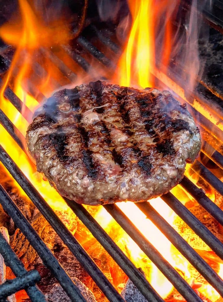 burger patty cooking over hot coals on a grill