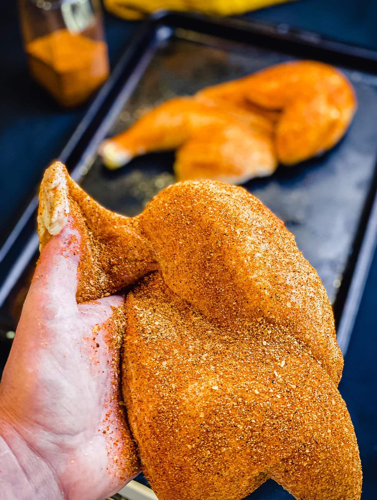 chicken half being seasoned under the wing