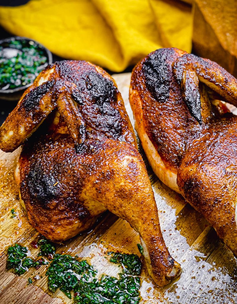 Grilled chicken halves on a cutting board with chimichurri sauce