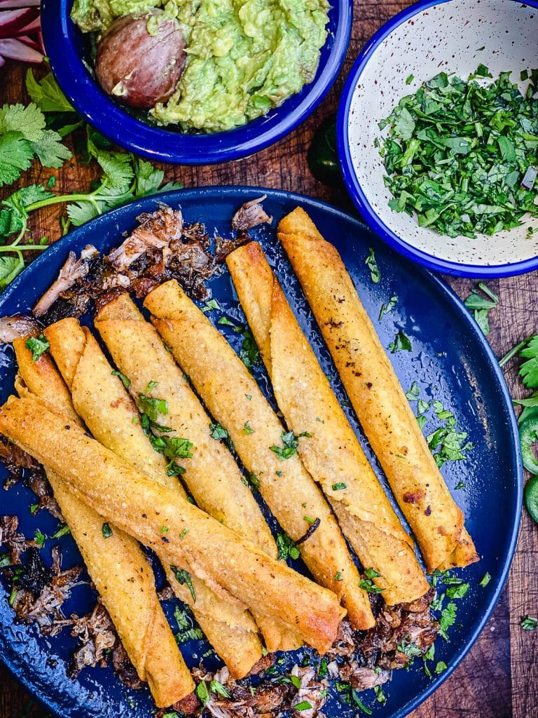 pile of taquitos on a blue plate with cilantro