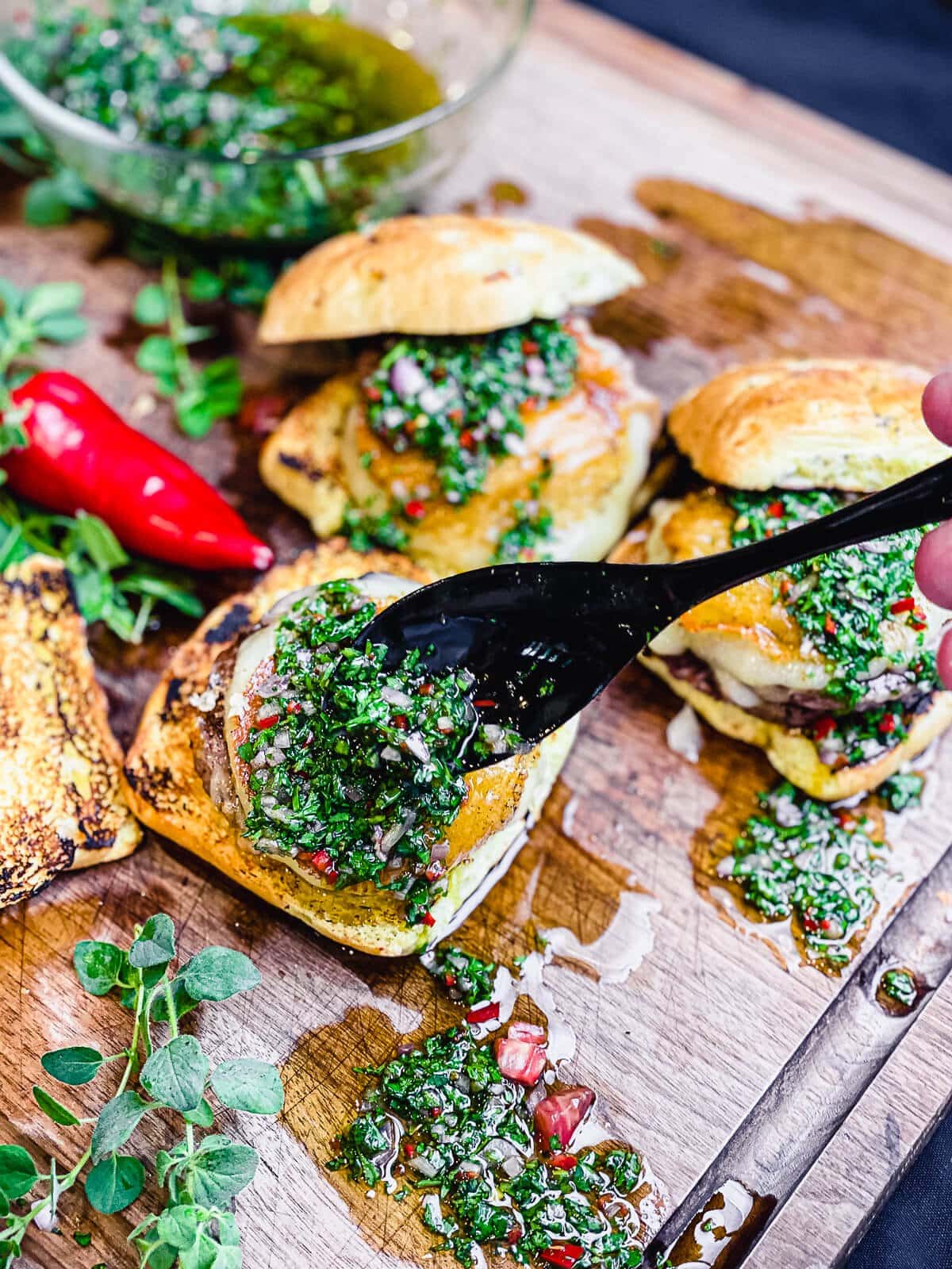 spoon dripping chimichurri onto a provoleta burger