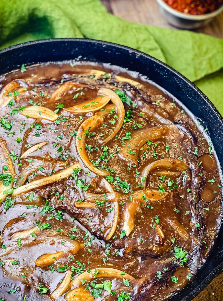 steaks in a cast iron pan cooking with gravy